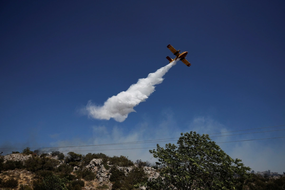 A plane drops water as firefighters try to extinguish a wildfire near the town of Koropi, Greece, June 19, 2024. REUTERS/Louisa Gouliamaki