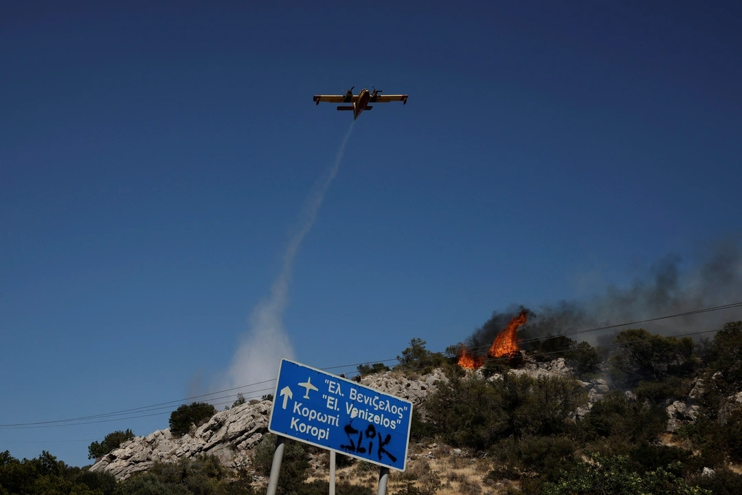 A plane drops water as firefighters try to extinguish a wildfire near the town of Koropi, Greece, June 19, 2024. REUTERS/Louisa Gouliamaki