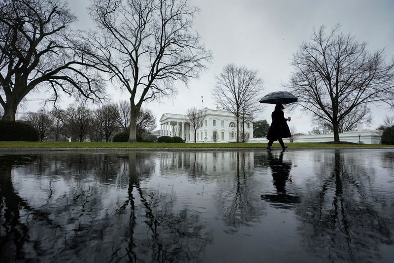 A reporter, arriving for work, walks up the driveway toward the White House on a rain-soaked morning in Washington, U.S., January 9, 2024. REUTERS/Kevin Lamarque