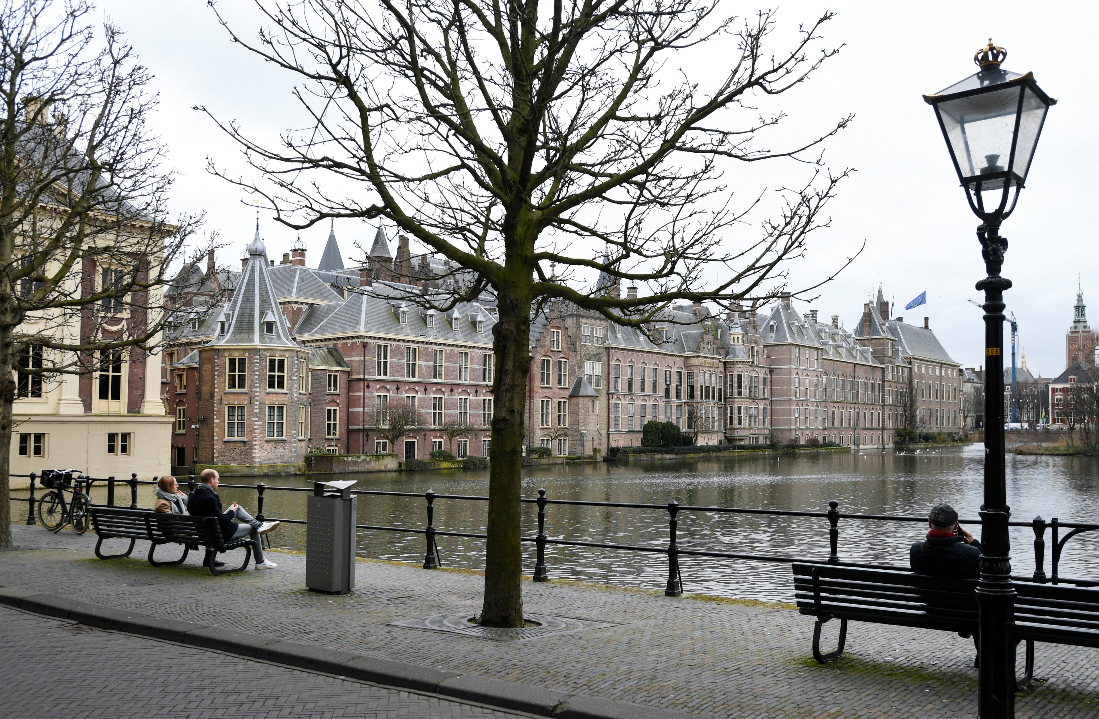 FILE PHOTO: People sit on benches with a view of the parliament building in The Hague, Netherlands March 9, 2021. Picture taken March 9, 2021. REUTERS/Piroschka van de Wouw/File Photo